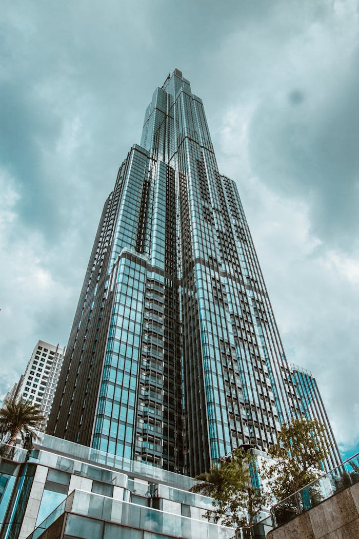 A towering, modern skyscraper with a glass facade under a dramatic cloudy sky, showcasing urban architecture.